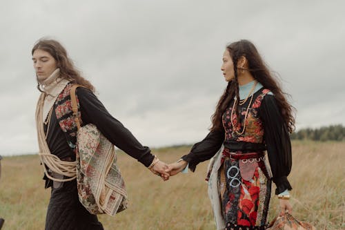 Man and Woman Walking on Green Grass Field while Holding Hands