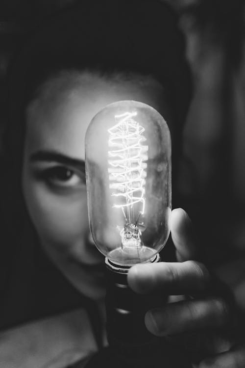 Grayscale Photo of a Person Touching a Light Bulb