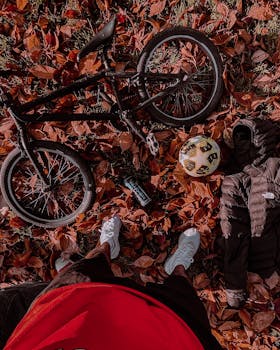 Bicycle amidst fallen leaves with sneakers and a jacket, capturing autumn vibes.