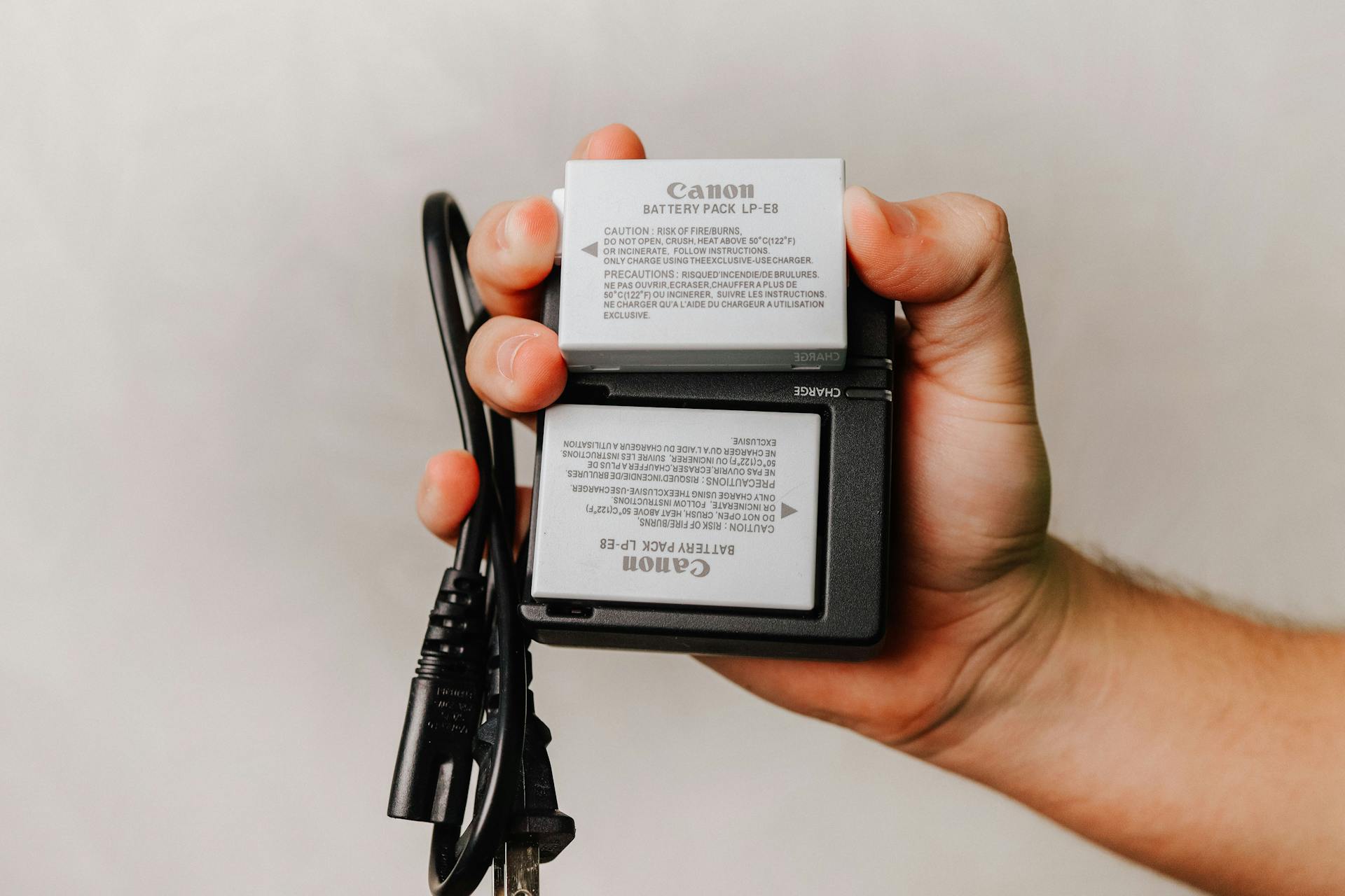 Close-up of a hand holding a Canon battery charger with cables, essential for photography electronics.