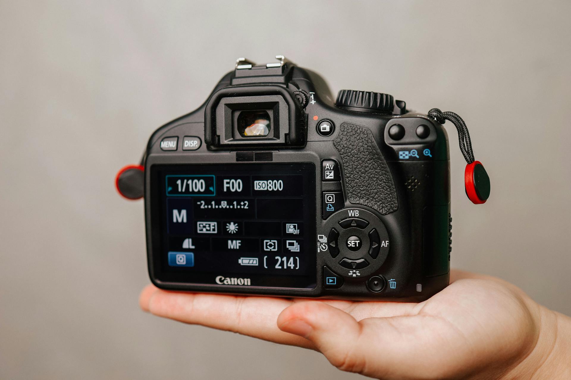 A close-up image of DSLR camera settings on display, held in adult hand.