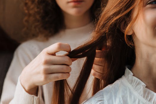 Two women bonding as one braids the other's hair, symbolizing friendship and beauty.