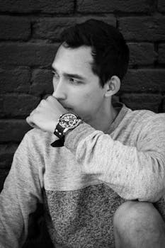 一名男子以深思熟虑的姿势，在砖墙背景下拍摄的单色肖像