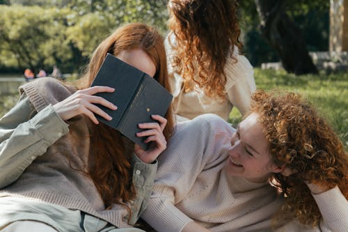 Female Friends Reading Book and Laughing in Park