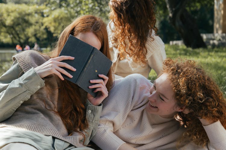 Female Friends Reading Book And Laughing In Park