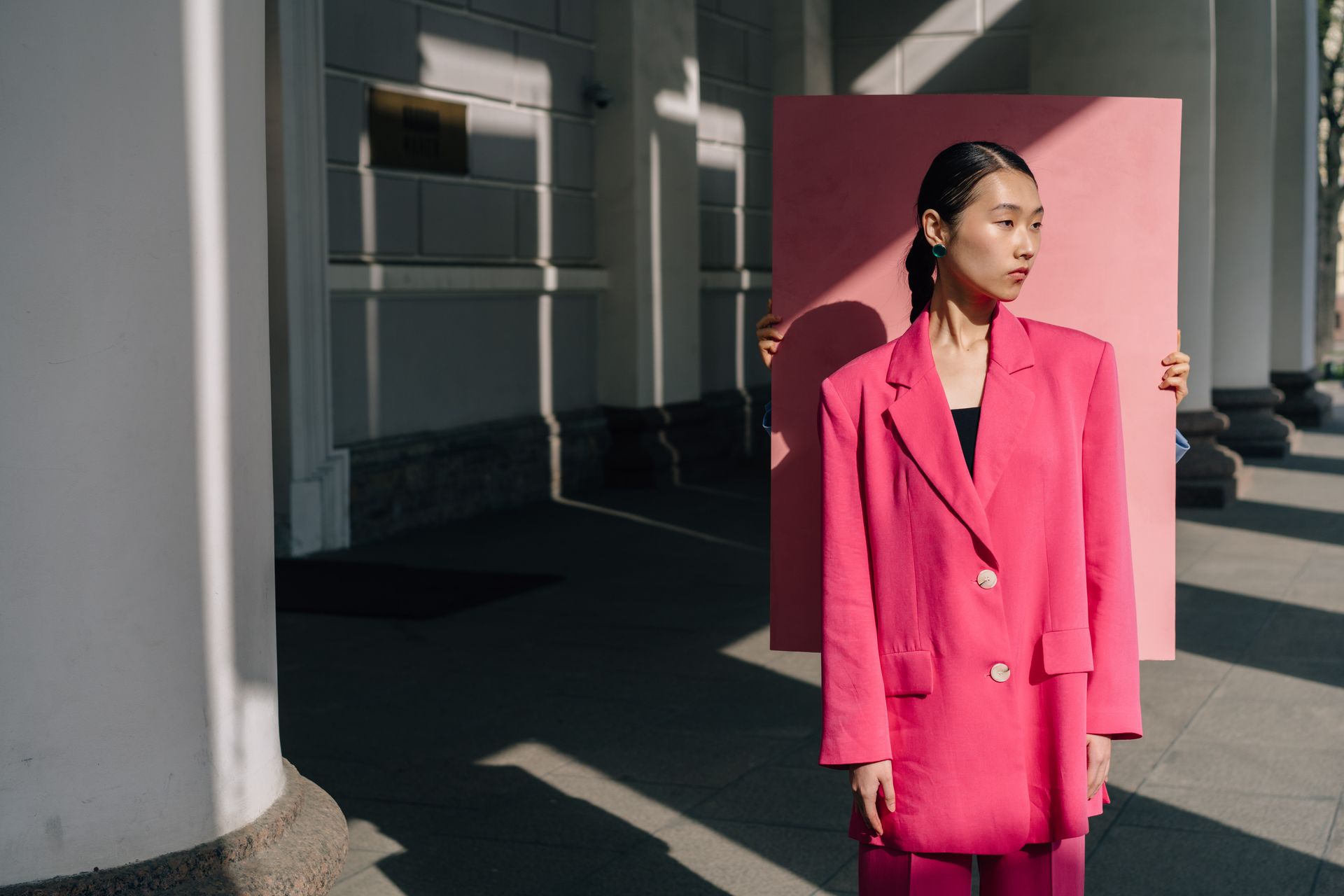 Person Holding a Pink Sheet Behind a Woman in Pink Blazer