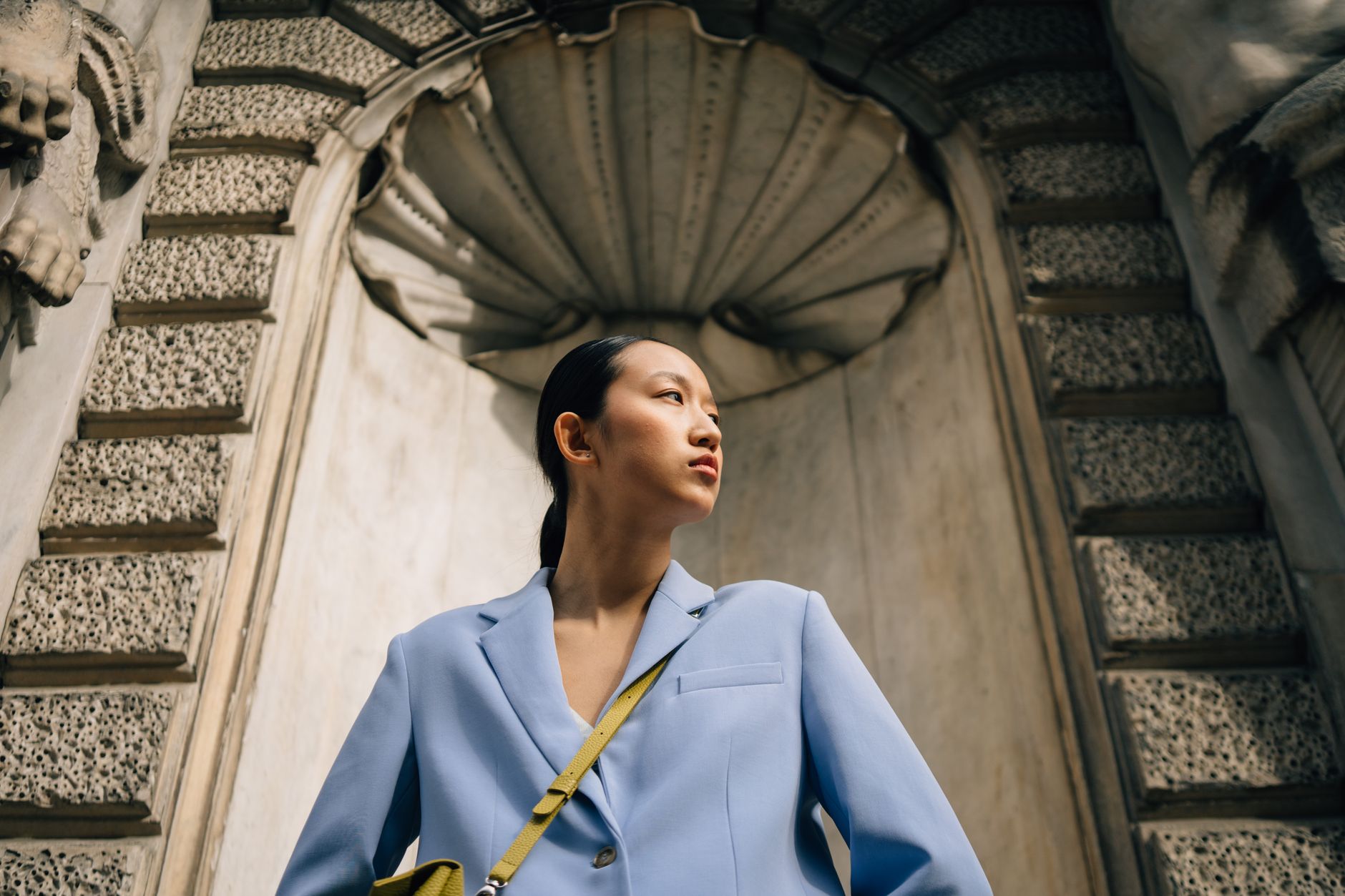 Stylish woman in blue suit posing against ornate urban architecture.