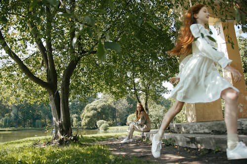 A Woman Sitting on Concrete Step Looking at a Girl in White Dress Running