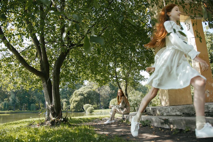 A Woman Sitting On Concrete Step Looking At A Girl In White Dress Running