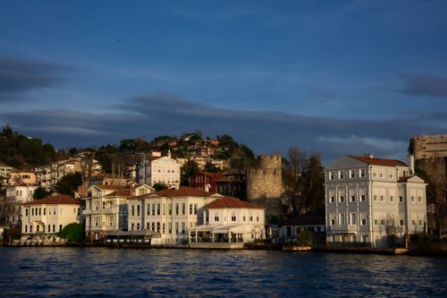 Free Charming waterfront buildings with historic castle ruins under a clear sky. Stock Photo