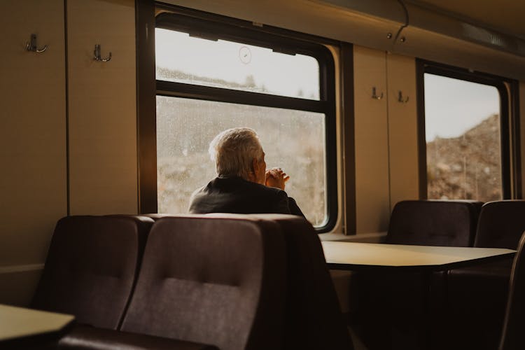 Elderly Man Travelling By Train And Seating By The Table 