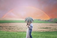 一对夫妇在风景优美的彩虹乡村，撑着伞接吻