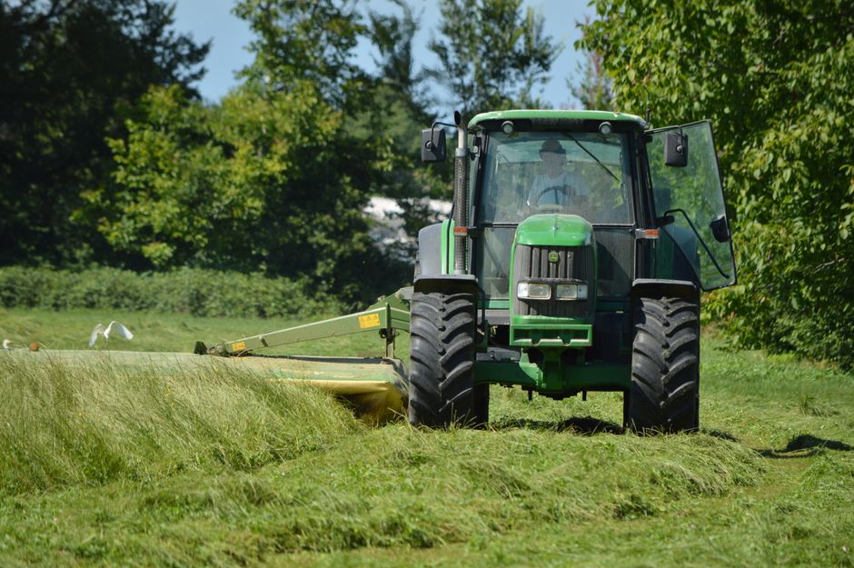 A green tractor plowing a field under a clear blue sky during daylight.
