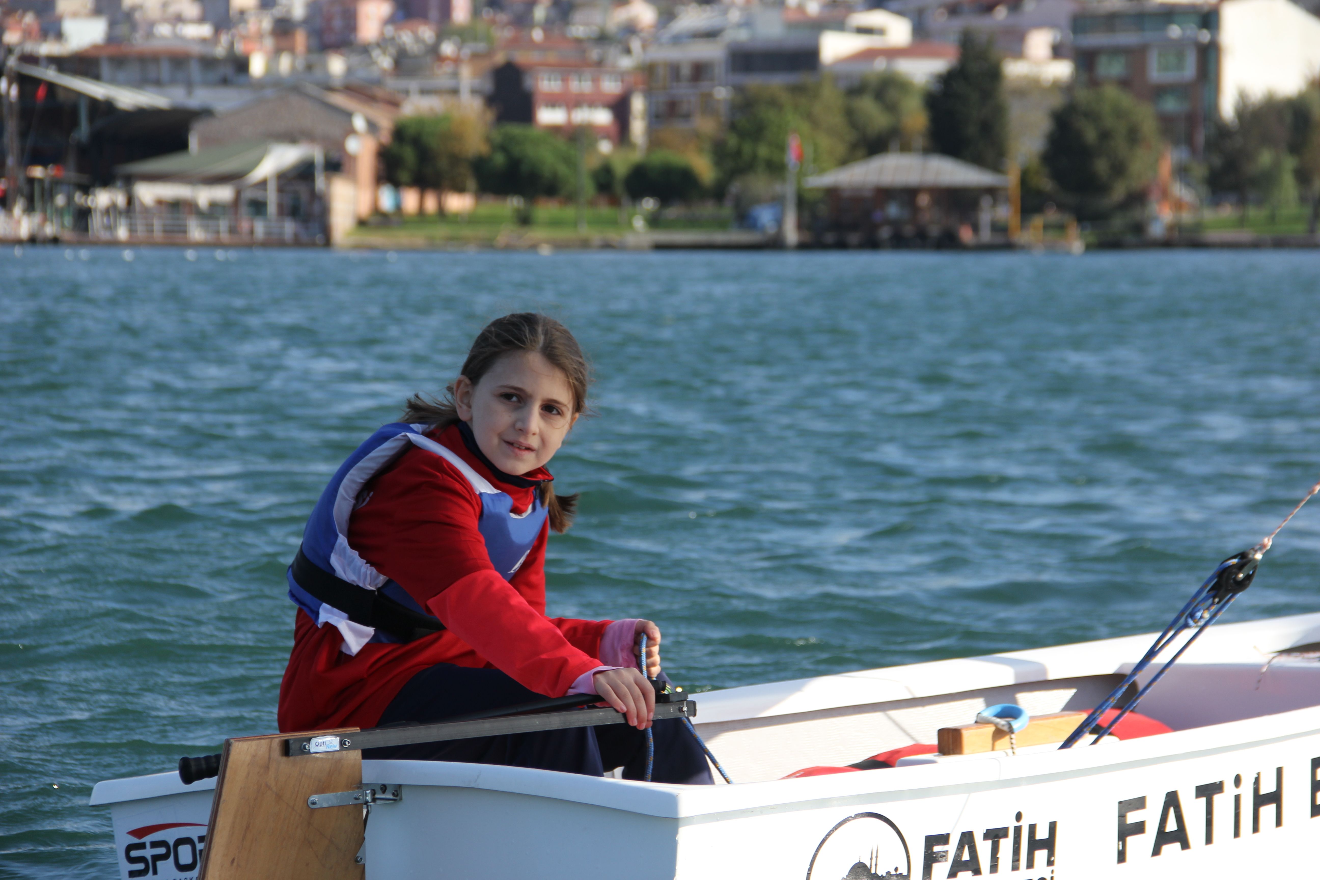 A young girl in a life vest enjoys boating on a sunny day, showcasing adventure and outdoor fun.