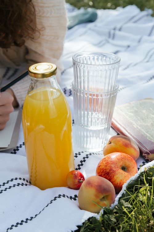 Free Sunny outdoor picnic with fresh juice and fruits on a blanket for relaxation. Stock Photo
