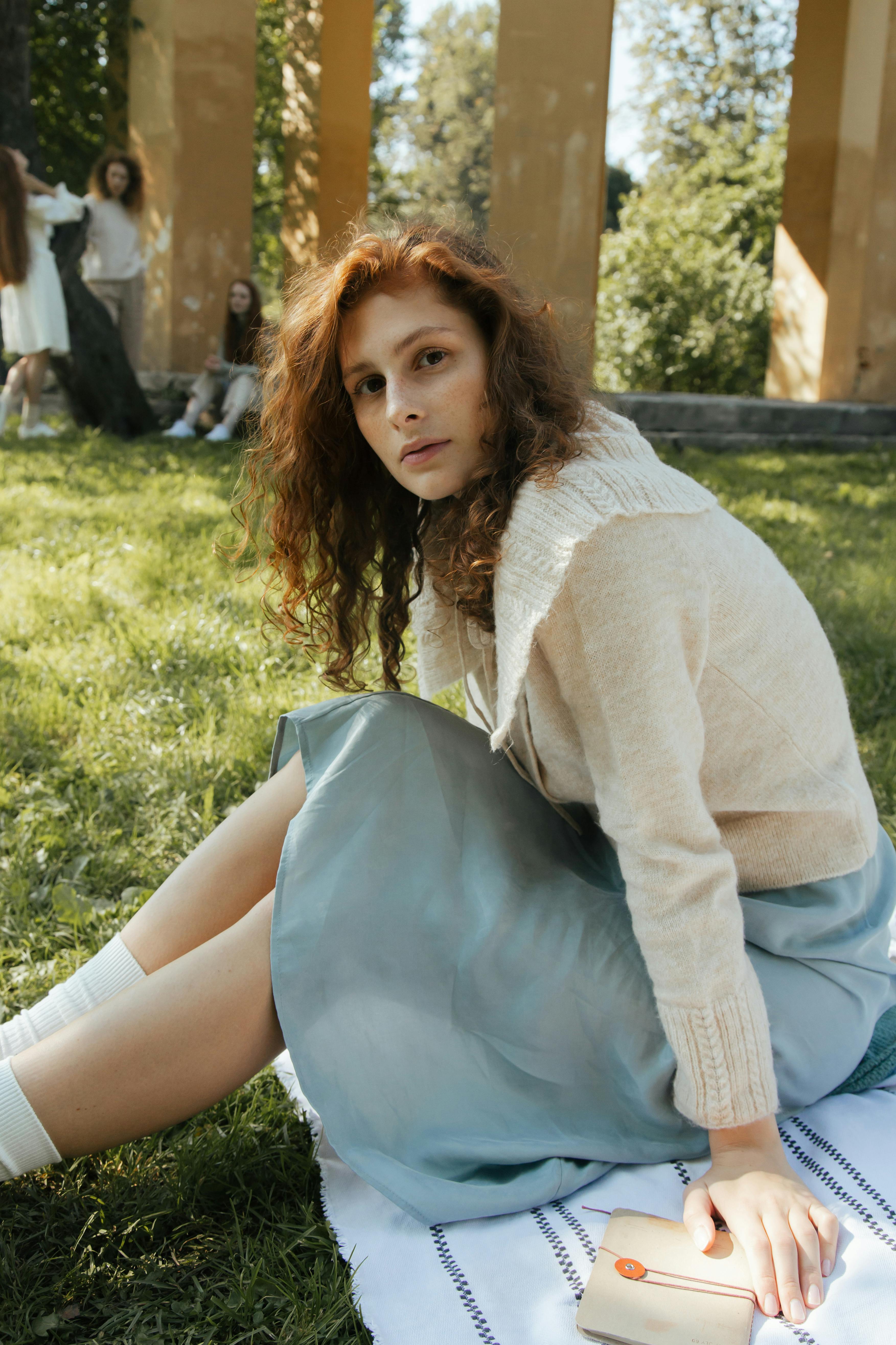 Woman enjoying a sunny day, sitting in a park with greenery and architectural elements.