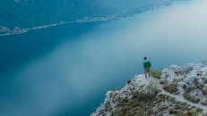 在意大利维罗纳，一名男子站在悬崖边，俯瞰着平静的湖泊，享受着宁静的风景