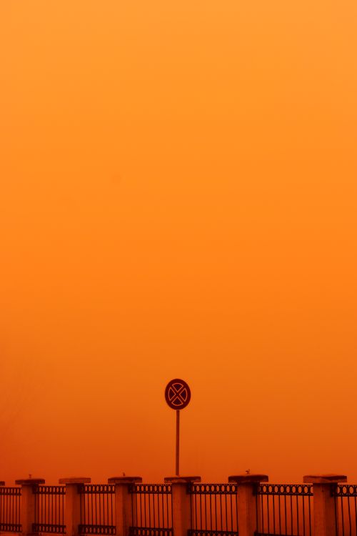 Free A 'no parking' sign stands against a vivid orange sky above a bridge in Edirne, Turkey. Stock Photo