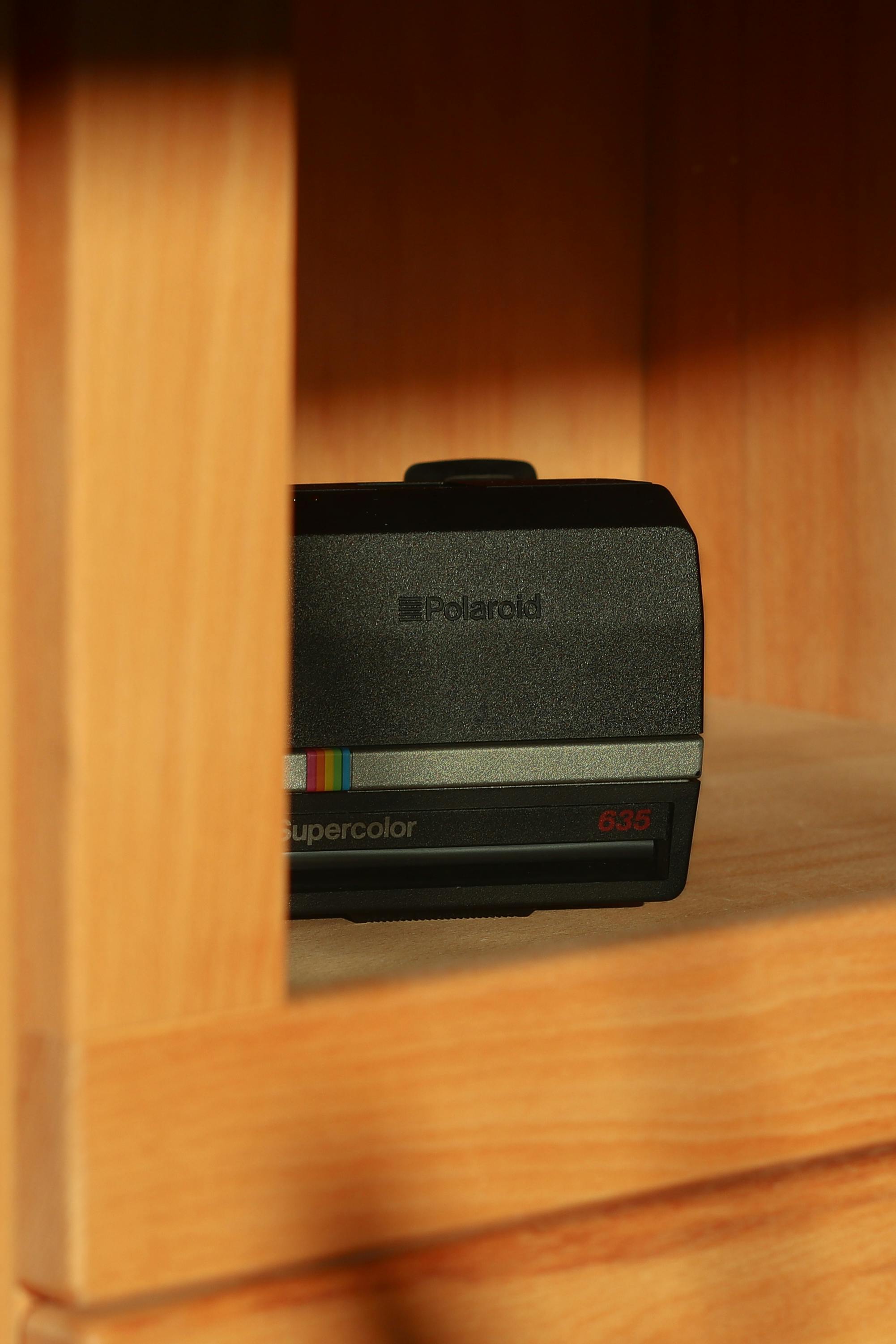 Close-up of a vintage Polaroid camera placed on a wooden shelf, bathed in sunlight.