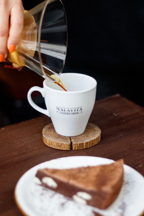 Free A close-up shot of coffee being poured into a cup with a slice of cake in the foreground. Stock Photo