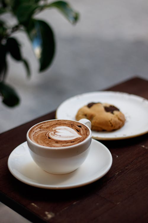 Free Latte Coffee in White Ceramic Cup Beside a Cookie on Saucer Stock Photo