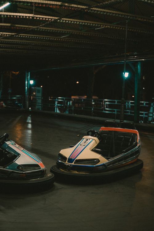 Free Two colorful bumper cars sit idle under dim amusement park lights at night. Stock Photo