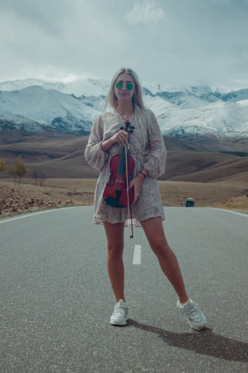 A Woman Standing on the Road while Holding a Violin