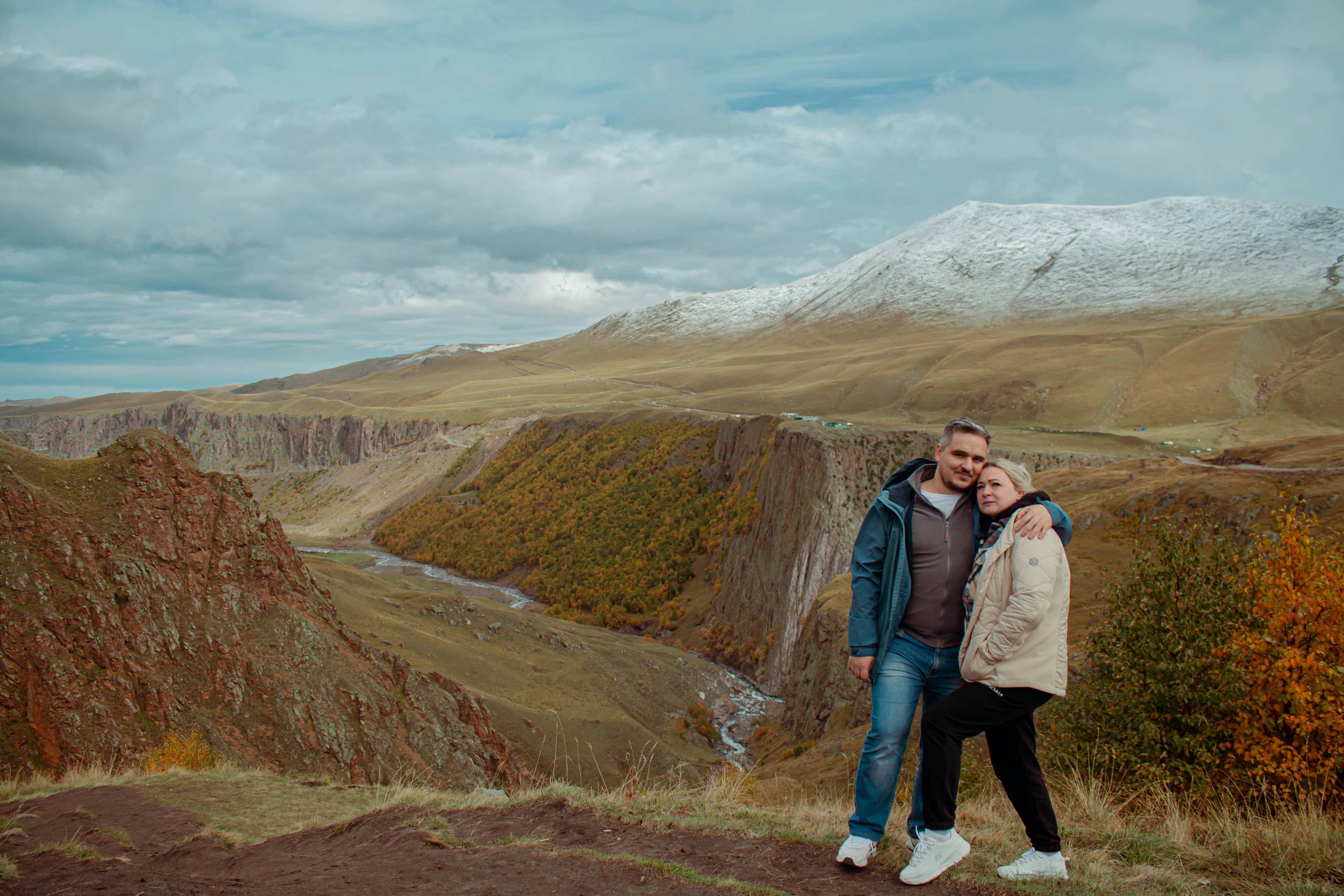 Couple embracing amidst a breathtaking mountain landscape in autumn.