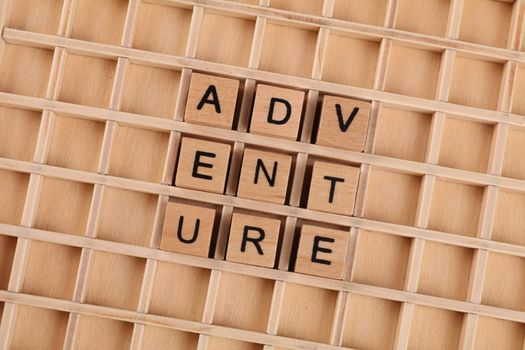 Wooden blocks arranged to spell 'Adventure' on a grid background.