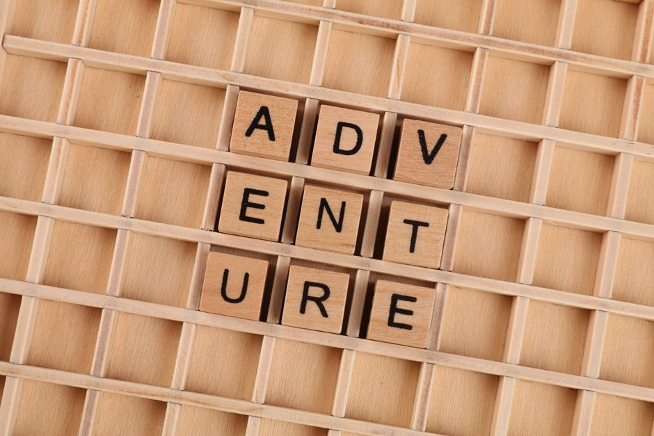 Wooden blocks arranged to spell 'Adventure' on a grid background.