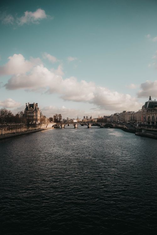 Free Tranquil river scene featuring historic bridges and cityscape under a blue sky with clouds. Stock Photo