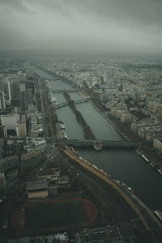 Dramatic aerial view of Paris with river, bridges, and cityscape under a moody sky.
