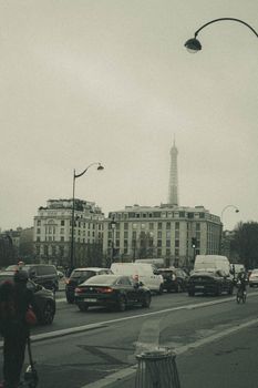 Urban scene of a busy Paris street in overcast weather with the Eiffel Tower visible.