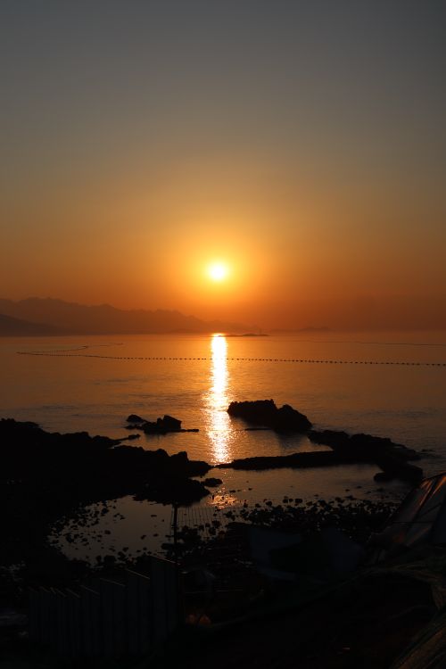 Free Captivating sunset view over a tranquil ocean with silhouetted rocks and orange skies. Stock Photo