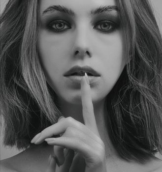 Elegant black and white portrait of a woman making a shh gesture with her finger.