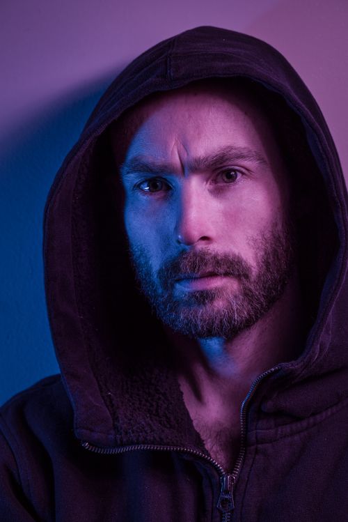 Free Portrait of a contemplative man in a hoodie under dramatic colored lighting. Stock Photo