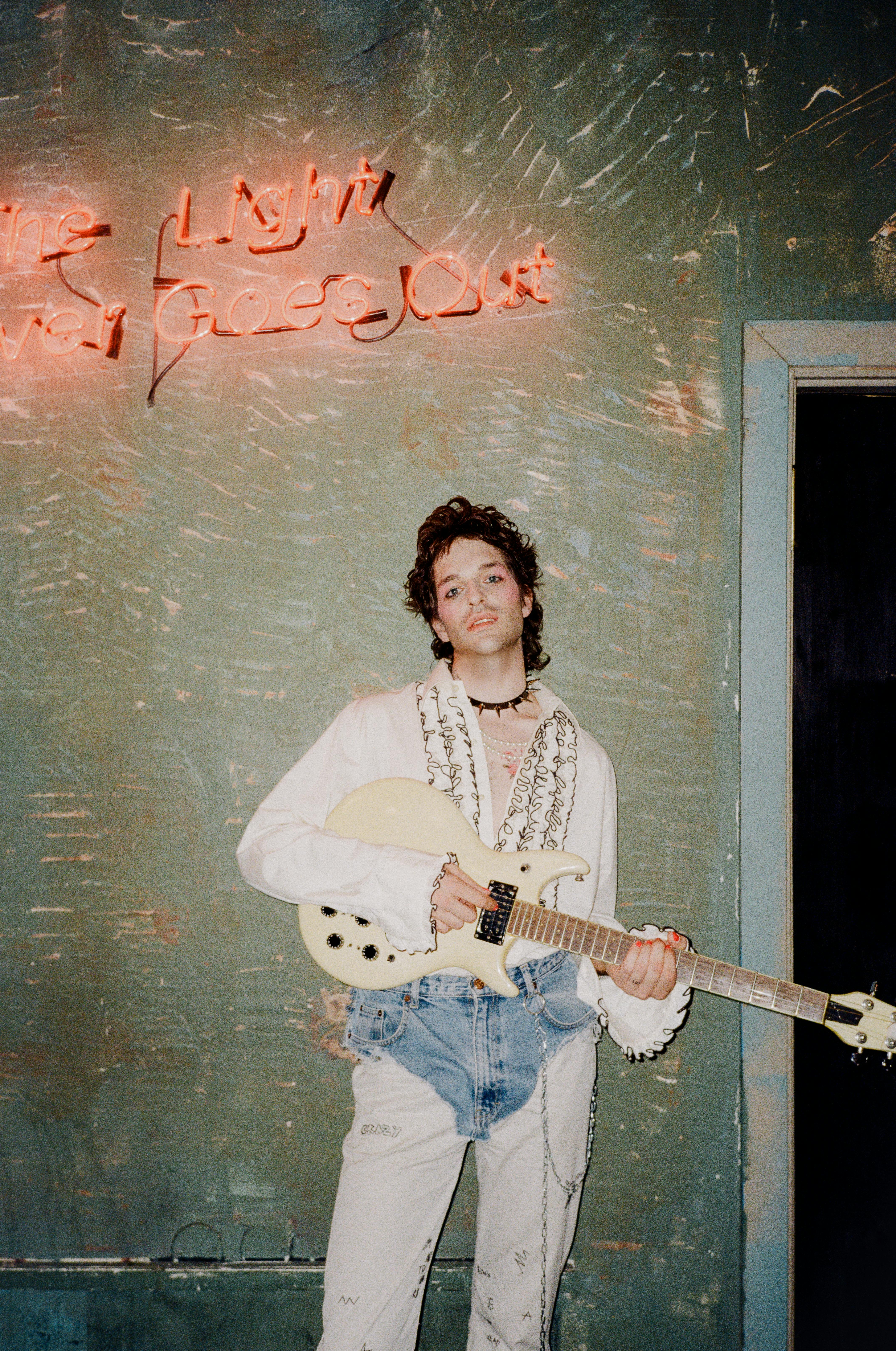 A fashionable musician holds an electric guitar against a neon-lit wall, exuding a vibrant punk style.