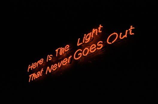 A glowing neon sign reads 'Here is the light that never goes out'.