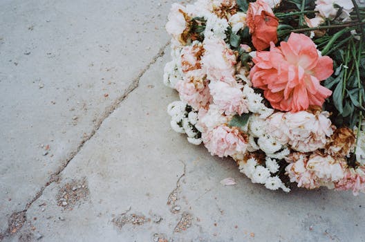 A close-up of a colorful arrangement of pink and white roses and daisies on a concrete surface.