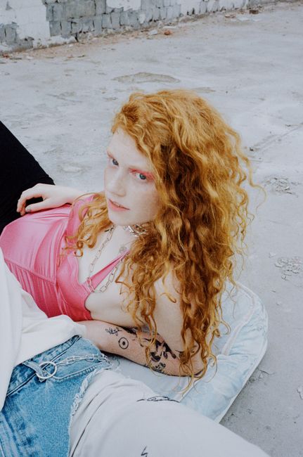 Artistic portrait of a red-haired woman with curly hair posing outdoors in casual fashion.