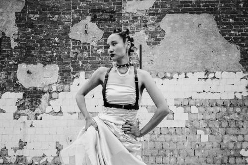 Free Black-and-white portrait of a stylish woman in a punk-inspired outfit against a deteriorating brick wall. Stock Photo