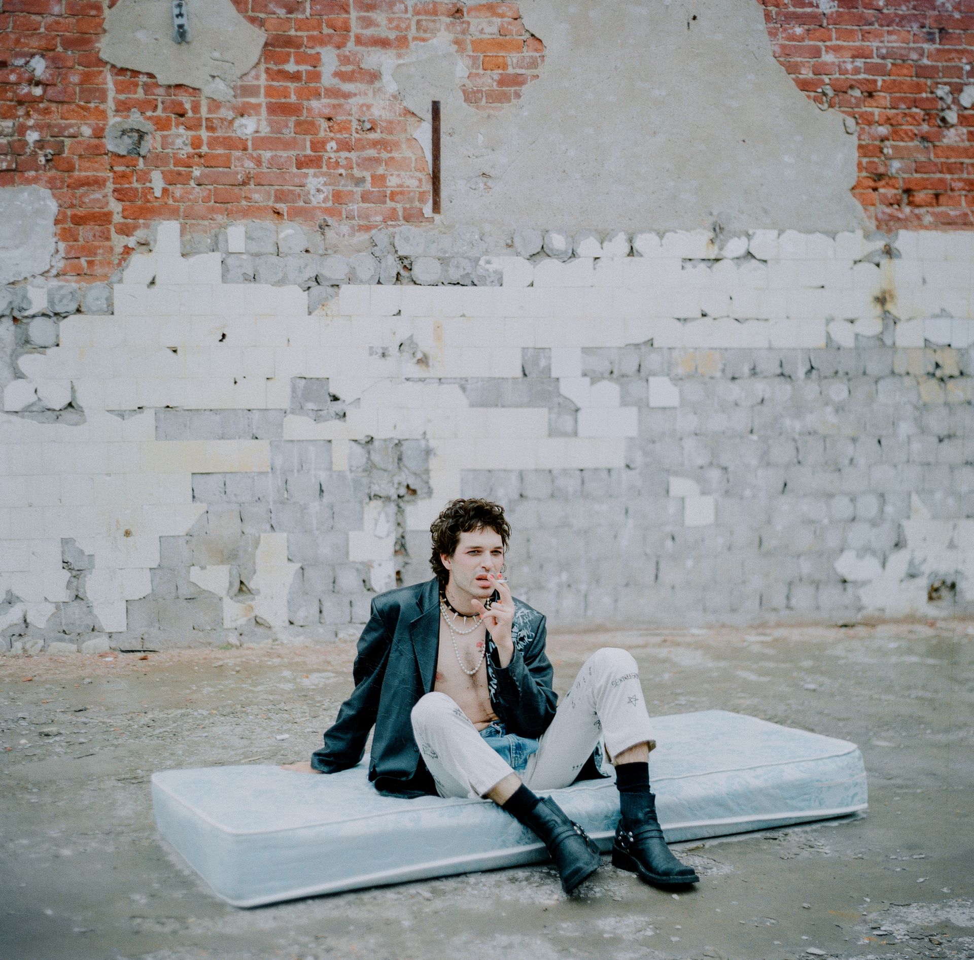 Man in Black Leather Jacket Sitting on Mattress while Smoking