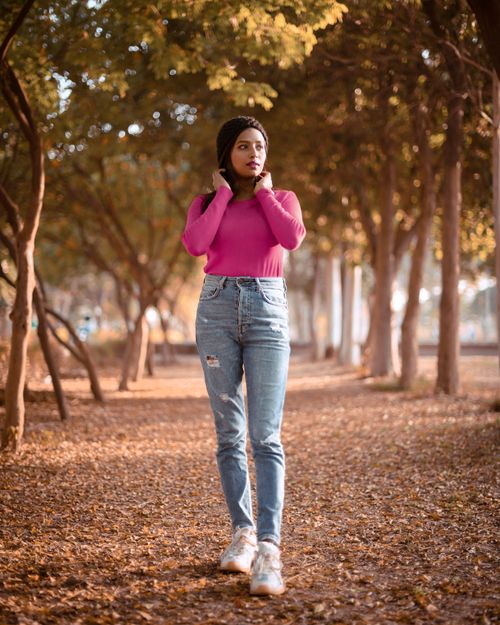 Free A woman in a pink sweater poses among fall trees in an outdoor park setting. Stock Photo