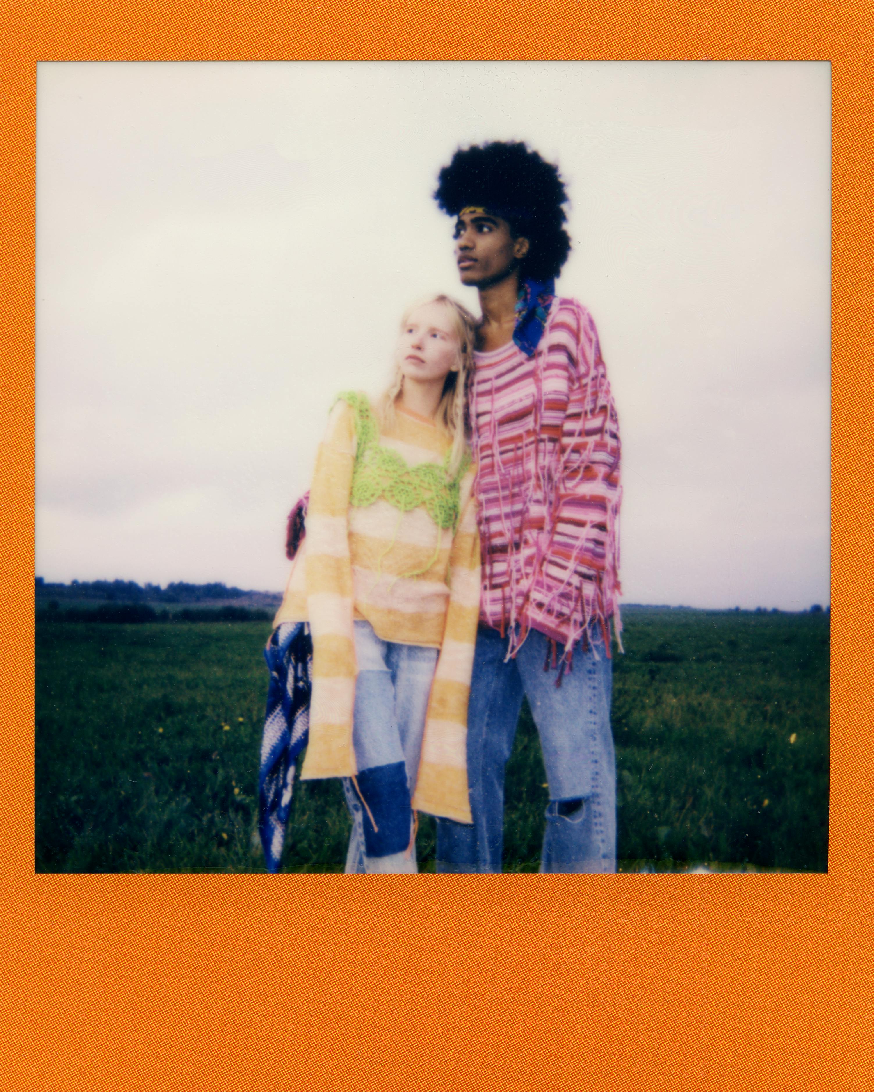 Young couple in colorful bohemian style clothing embracing in a rural meadow.