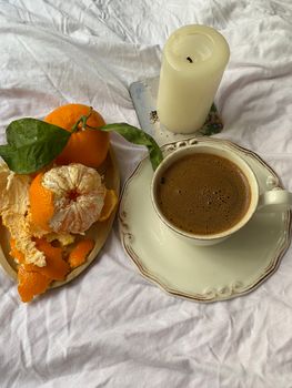 A warm breakfast scene featuring black coffee with fresh oranges and a lit candle.