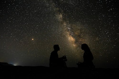 Free Silhouette of Sitting on the Ground while Facing Each Other Under Starry Sky Stock Photo