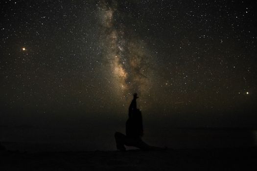 Person silhouetted against the Milky Way in a starry night sky.