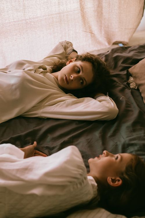 Free Two women lying on a bed, sharing a quiet and intimate moment in soft, natural light. Stock Photo