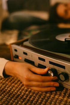 Close-up of hands adjusting a vintage vinyl record player, setting a warm, nostalgic mood.