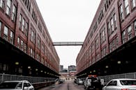 两座对称的砖砌建筑之间，可见一条停着汽车的城市小巷，背景是城市街景